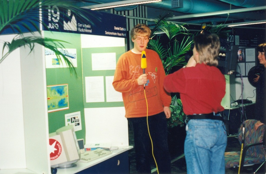 Daniel is being interviewed in front of his exhibit