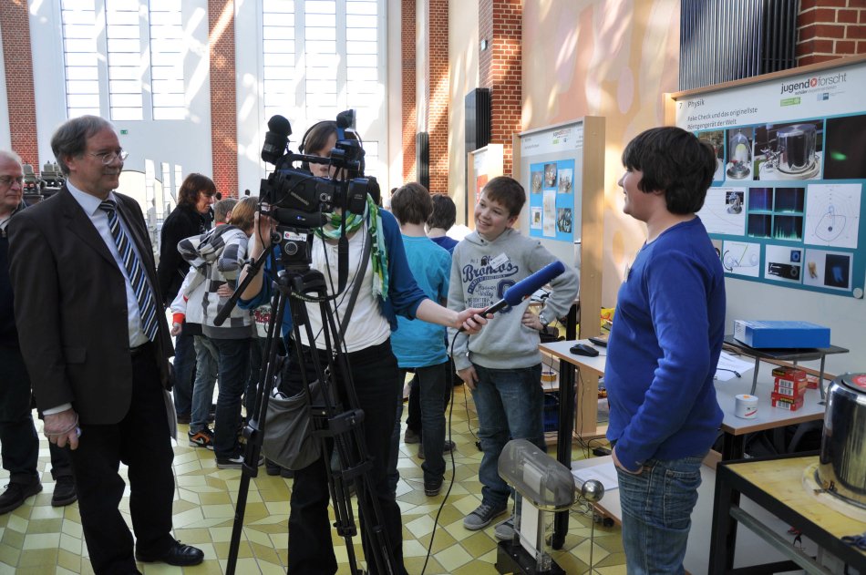 Lukas and Leon are being interviewed by a TV channel while principal Paul Georg Neft is watching